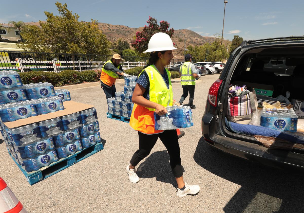 Un trabajador en chaleco y sombrero duro lleva uno de los muchos casos de agua embotellada a un automóvil.