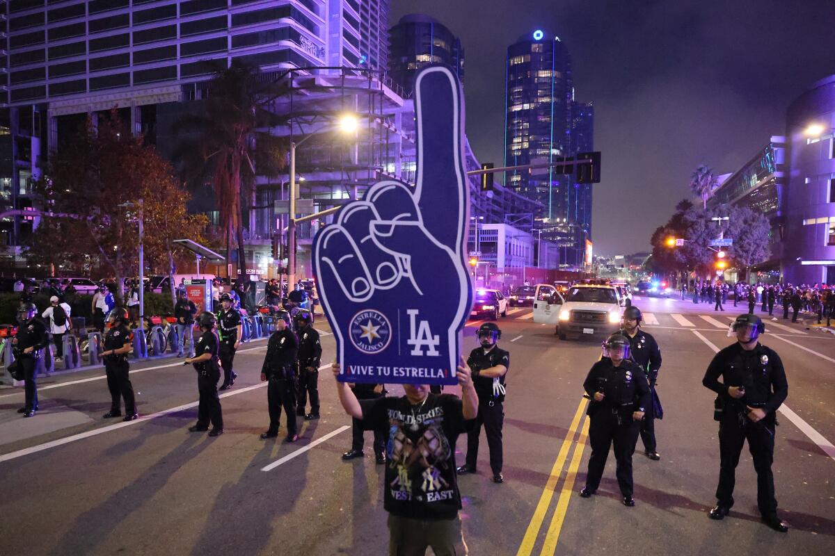 Una persona sostiene un dedo gigante de espuma de los Dodgers cerca de una fila de agentes de policía.